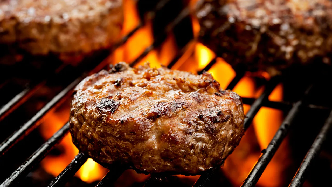 Closeup of tongs gripping a burger cooking over a grill